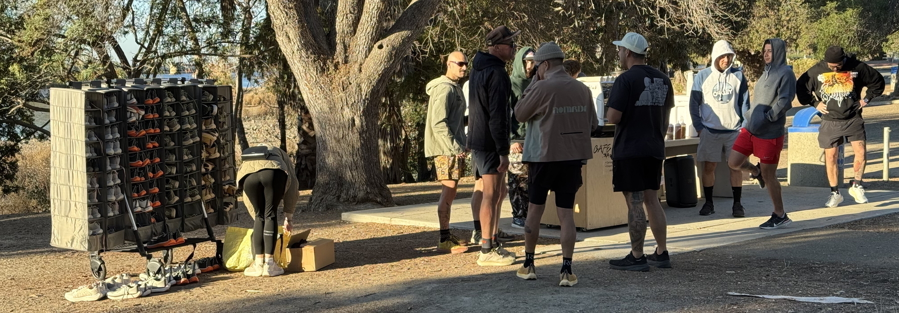 A group of men and maybe one woman gathered outdoors near a table and a rack filled with shoes in neat cubbies.