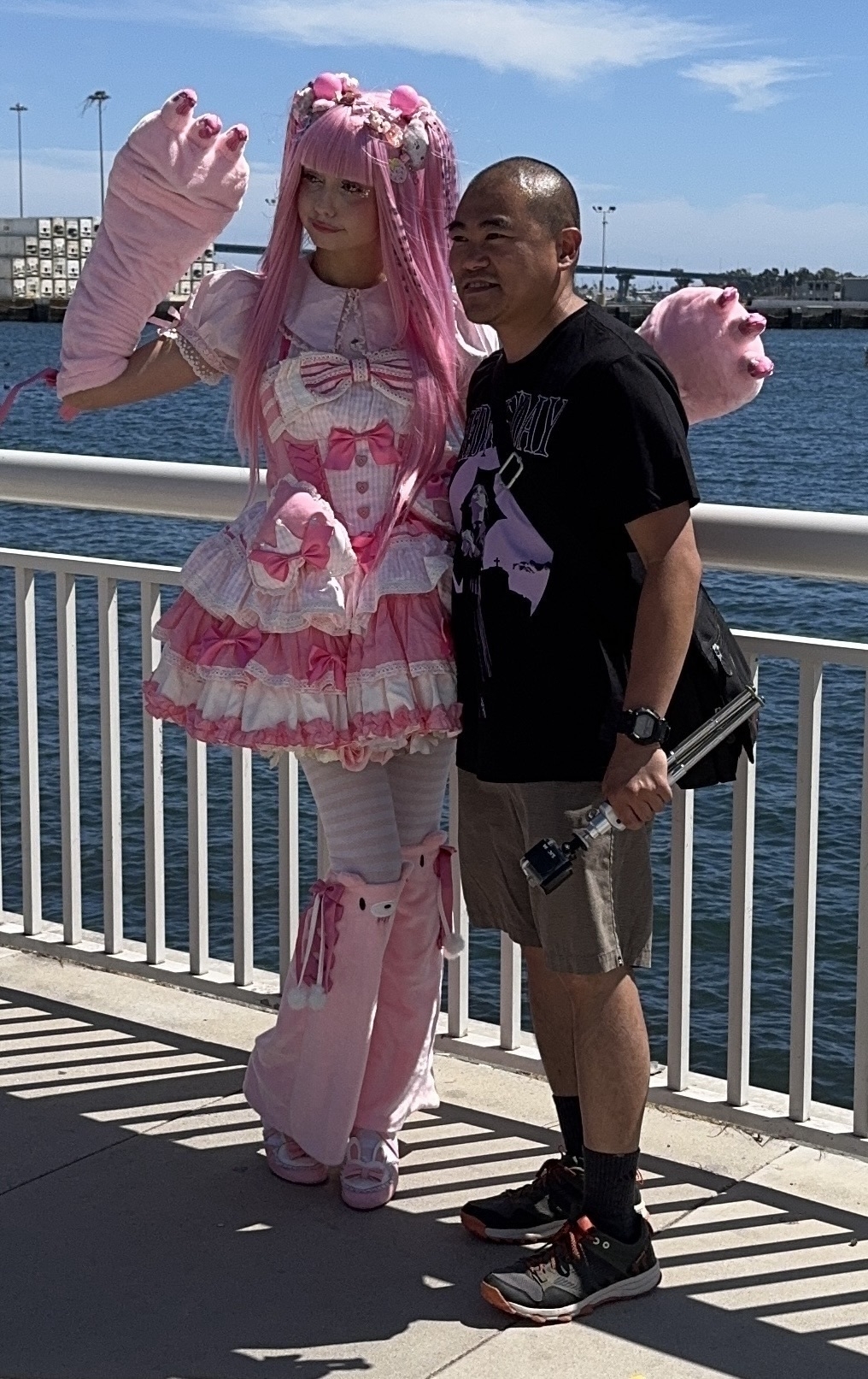 Auto-generated description: A person in a pink, frilly costume poses with a smiling man by a waterfront railing.
