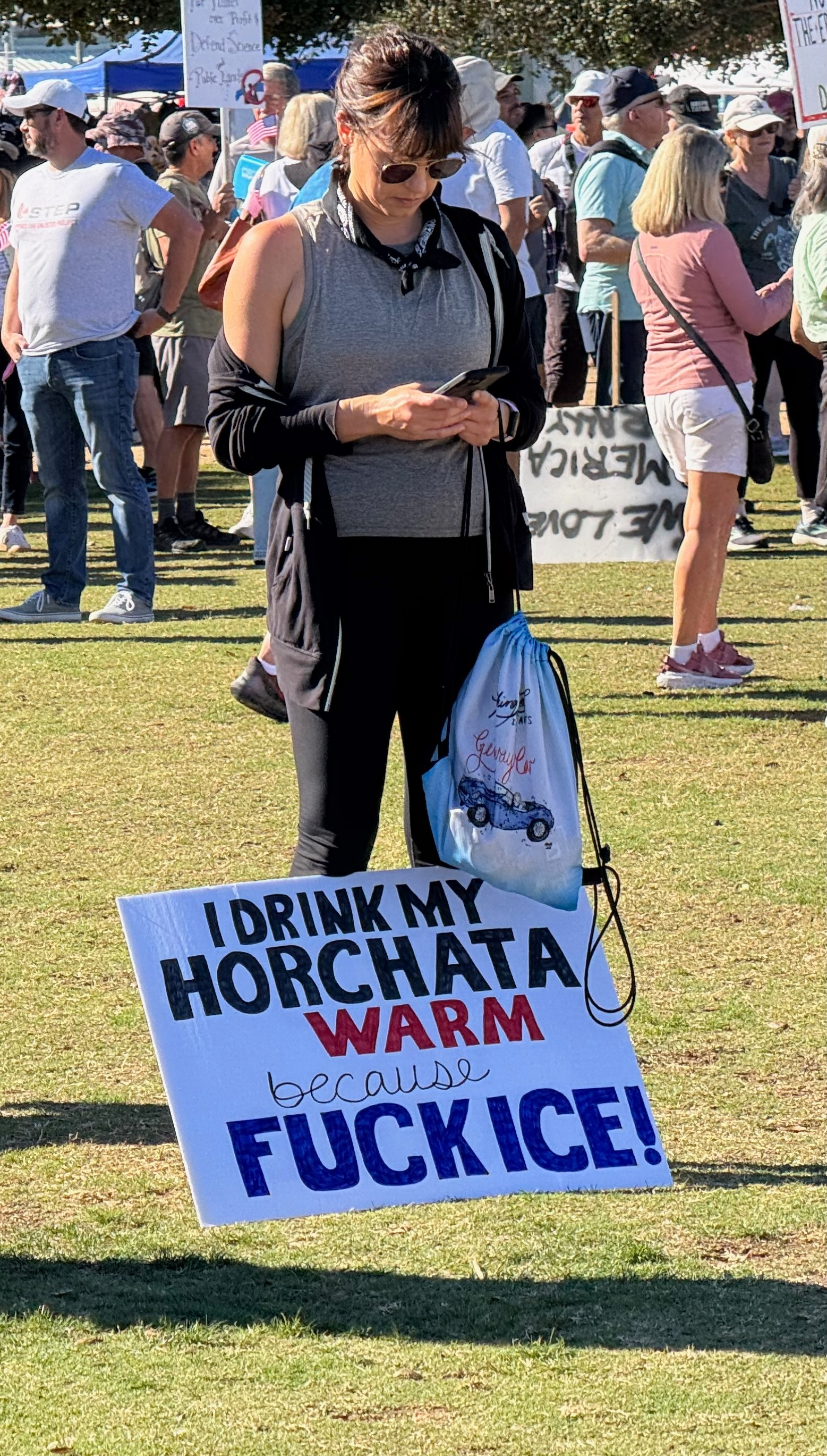 Auto-generated description: A woman stands in a crowd holding a sign that expresses a strong opinion about drinking warm horchata and a political stance on ICE.