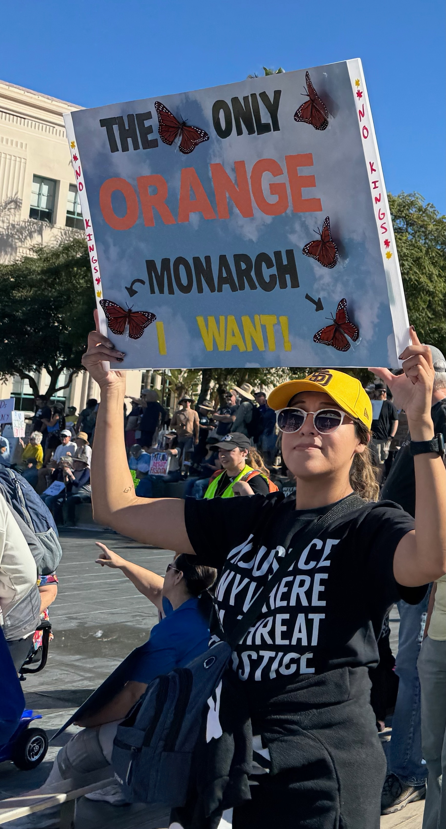 Auto-generated description: A person in a crowd holds a sign with butterflies that reads, THE ONLY ORANGE MONARCH I WANT!